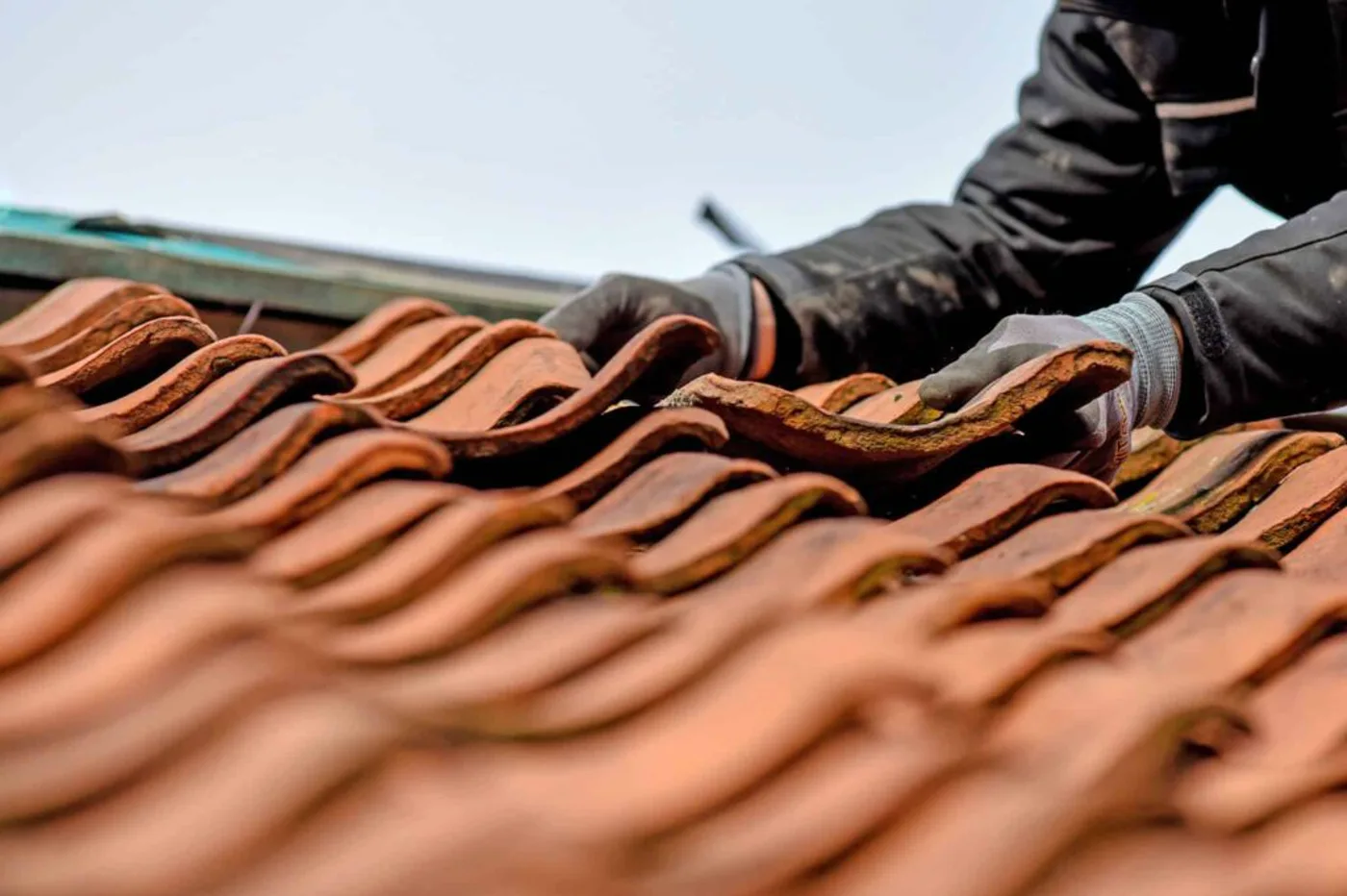 Dachdecker tauscht von Hand einen roten Dachziegel aus